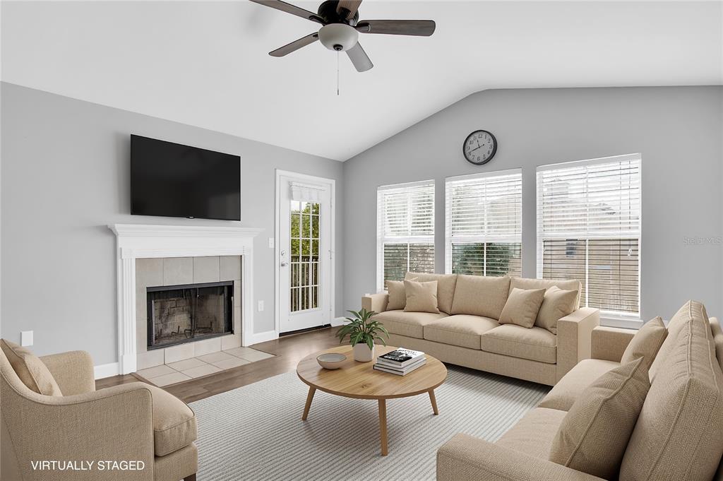 A living room features a fireplace, wood-look flooring, a ceiling fan, and three large windows — 18245 BRIDLE CLUB DRIVE, TAMPA, FL