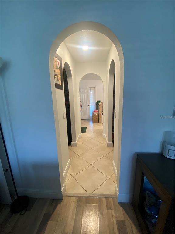 A hallway with arched entryways features tiled flooring and leads to a doorway at the end — 5287 SUNSET CANYON DRIVE, KISSIMMEE, FL