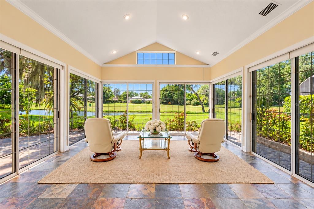 A sunroom with slate tile flooring, vaulted ceilings, and large glass walls overlooking a pond — 203 PRESTWICK DRIVE, NEW SMYRNA BEACH, FL