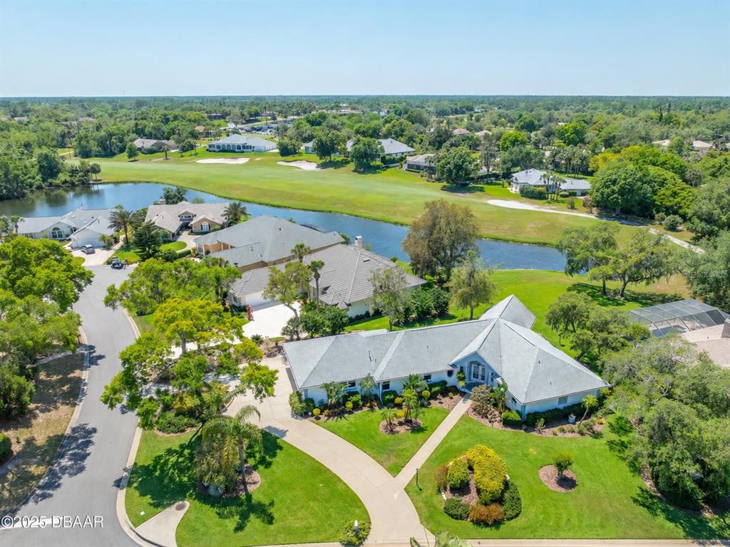 A spacious living room features vaulted ceilings, hardwood floors, and large windows overlooking a backyard — 203 PRESTWICK DRIVE, NEW SMYRNA BEACH, FL