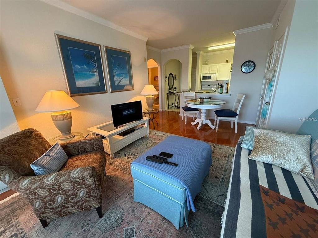 A living room with a patterned armchair, blue ottoman, television, and an adjacent dining area — 1216 S MISSOURI AVENUE UNIT 427, CLEARWATER, FL