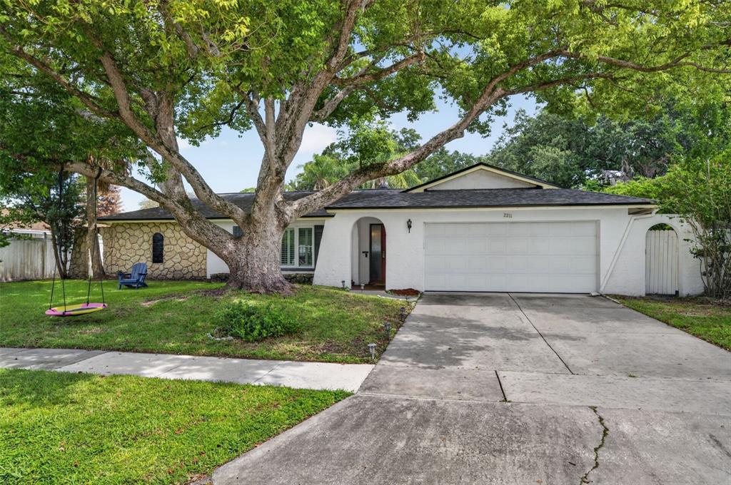 A single-story house with a white exterior, stone accents, a large tree, and a driveway — 2211 KING RICHARDS COURT, WINTER PARK, FL