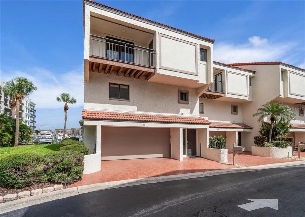 A multi-story townhouse exterior features a tan stucco facade, a garage, and a balcony — 240 WINDWARD PSGE UNIT 401, CLEARWATER BEACH, FL