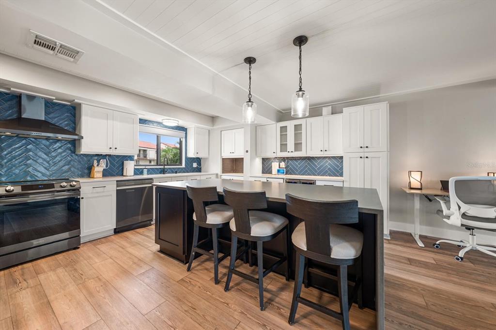 A modern kitchen features white cabinets, a dark island with bar stools, and blue backsplash — 240 WINDWARD PSGE UNIT 401, CLEARWATER BEACH, FL