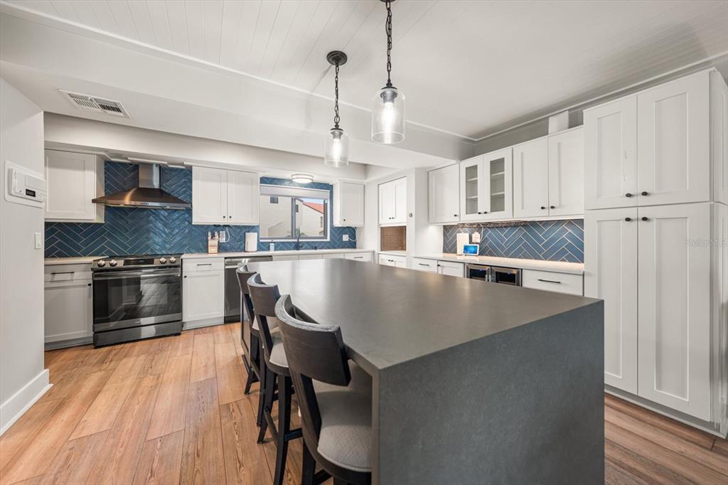 A modern kitchen features white cabinetry, a large dark island, and blue herringbone tile backsplashes — 240 WINDWARD PSGE UNIT 401, CLEARWATER BEACH, FL