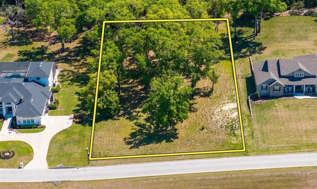 An aerial view shows a rectangular wooded lot outlined in yellow near a paved road — 7041 NORNE LANE, MOUNT DORA, FL