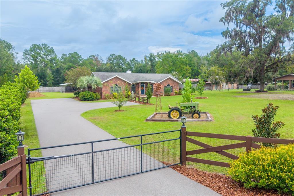 A brick house with a paved driveway, a metal gate, and a vintage tractor display — 11255 W COUNTY ROAD 18, LAKE BUTLER, FL