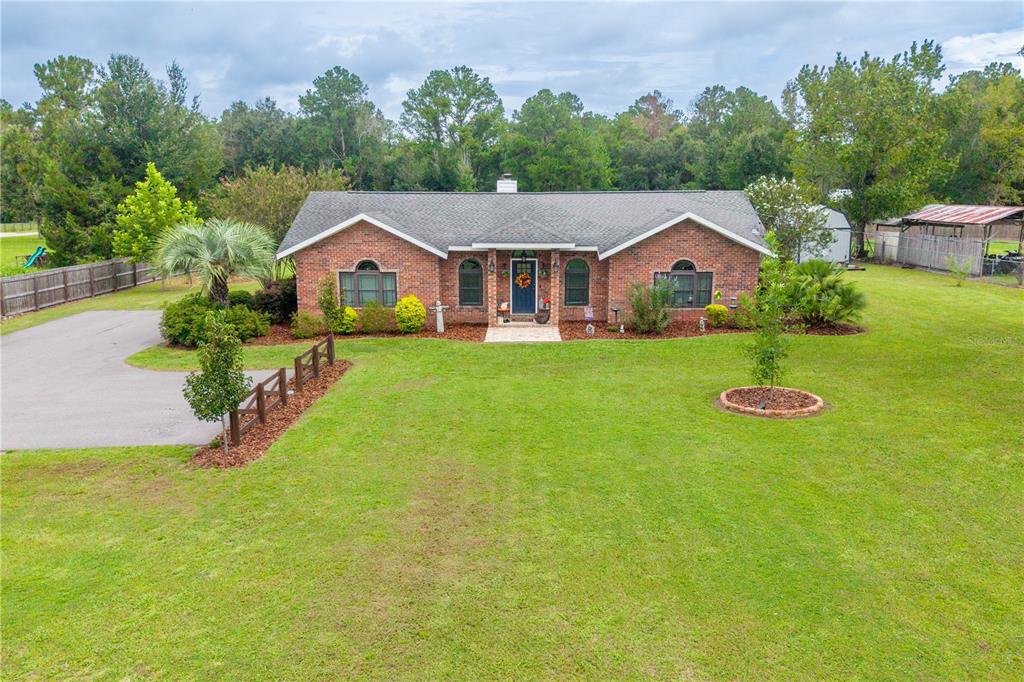 A single-story brick house with a gray shingled roof sits on a large grassy lawn — 11255 W COUNTY ROAD 18, LAKE BUTLER, FL