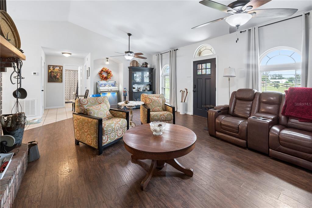 A living room features wood-look flooring, a brick fireplace, patterned armchairs, and a brown sofa — 11255 W COUNTY ROAD 18, LAKE BUTLER, FL