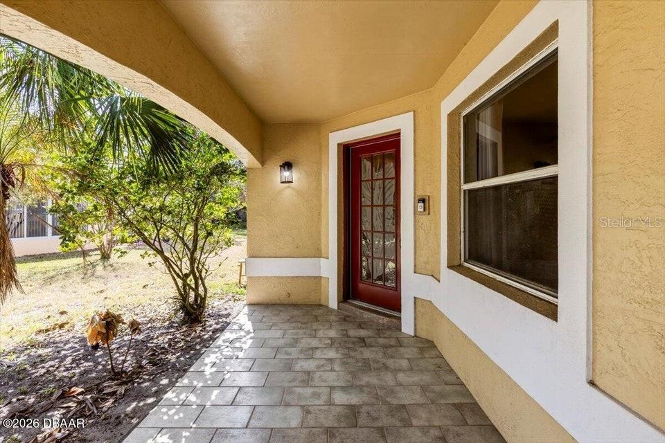 A covered front porch with tiled flooring leads to a red front door — 29 SHERRINGTON DRIVE, ORMOND BEACH, FL