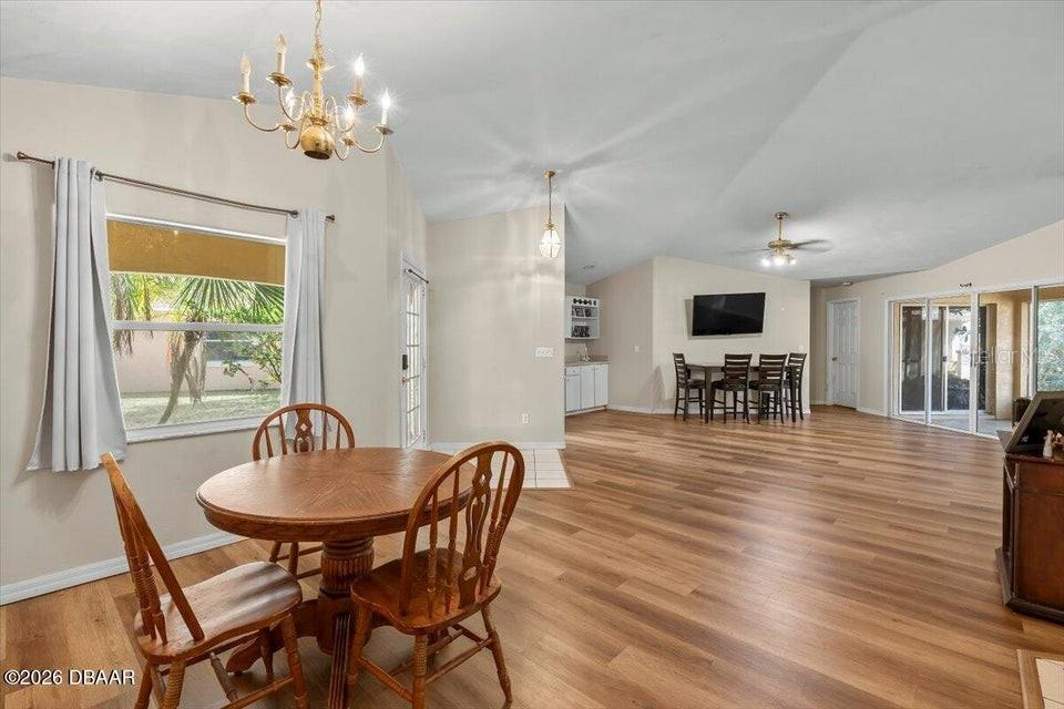 A dining area with a round wooden table and chandelier opens into a spacious living room — 29 SHERRINGTON DRIVE, ORMOND BEACH, FL