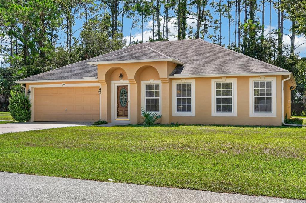 A single-story tan house with a two-car garage, arched entryway, and a grassy front yard — 99 PICKERING DRIVE, PALM COAST, FL