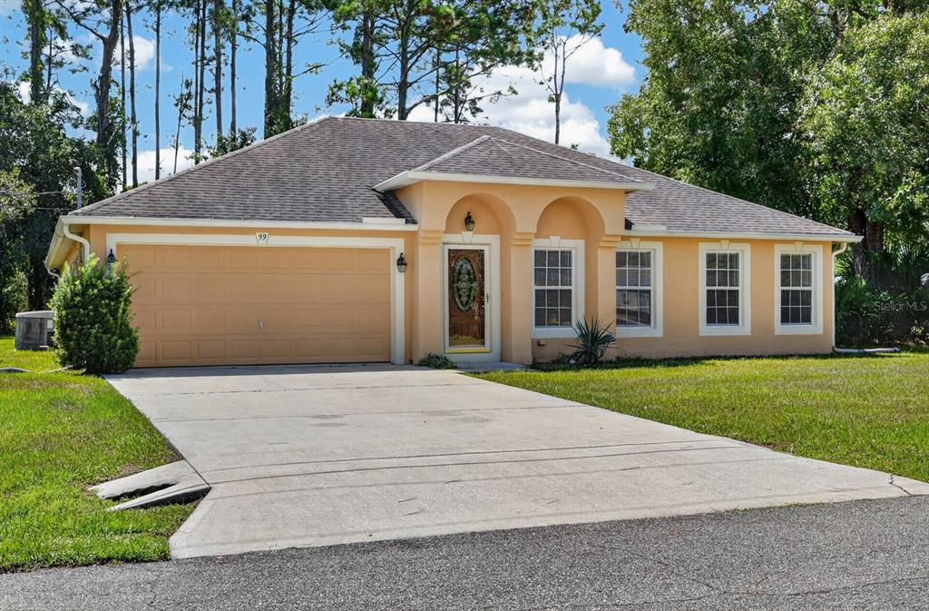 A single-story peach-colored house with a two-car garage, arched entryway, and a concrete driveway — 99 PICKERING DRIVE, PALM COAST, FL