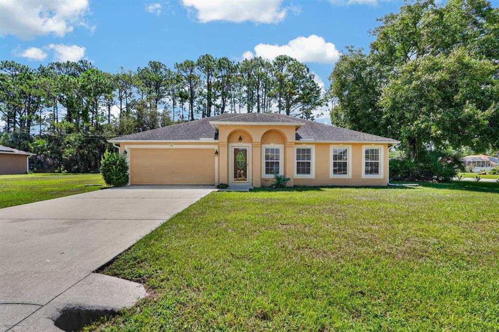 A single-story house with a tan stucco exterior, a two-car garage, and a front lawn — 99 PICKERING DRIVE, PALM COAST, FL