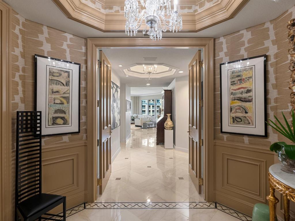 A formal foyer with marble floors, a crystal chandelier, and framed artwork on paneled walls — 35 WATERGATE DRIVE UNIT 906, SARASOTA, FL