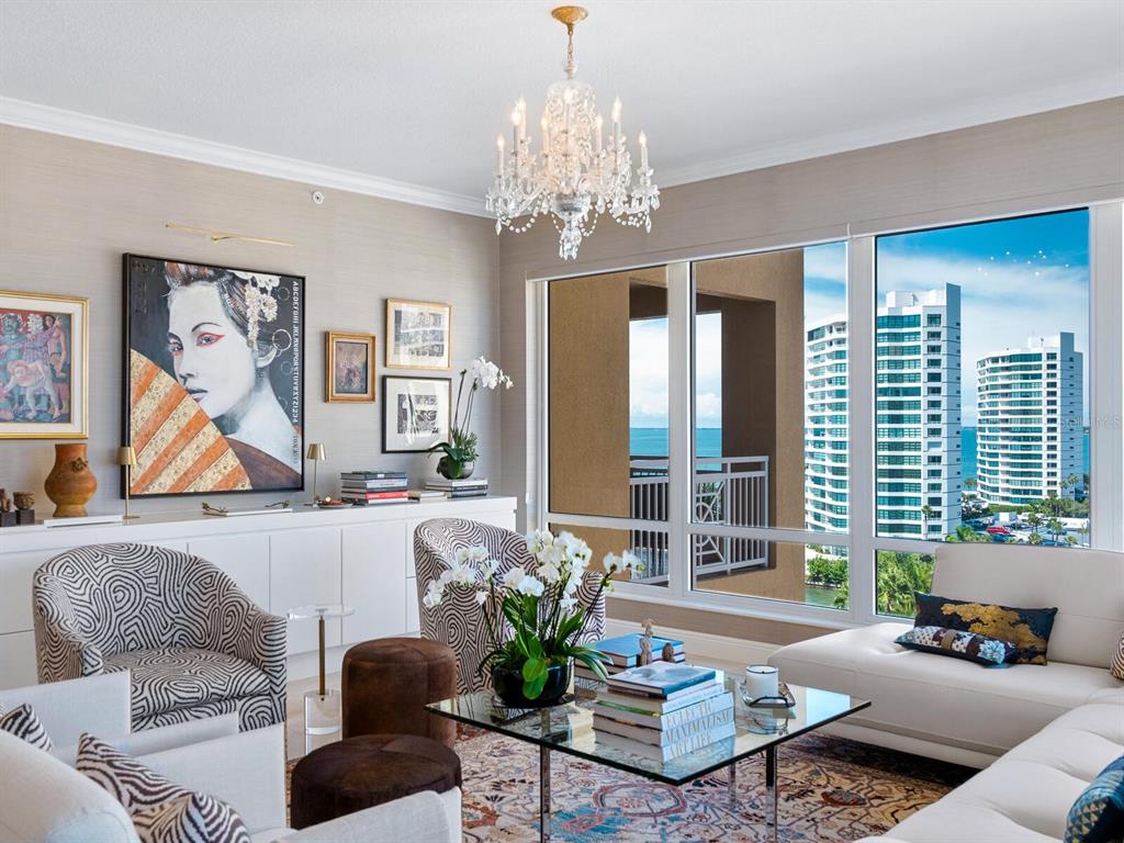 A bright living room features patterned armchairs, a glass coffee table, and floor-to-ceiling windows — 35 WATERGATE DRIVE UNIT 906, SARASOTA, FL