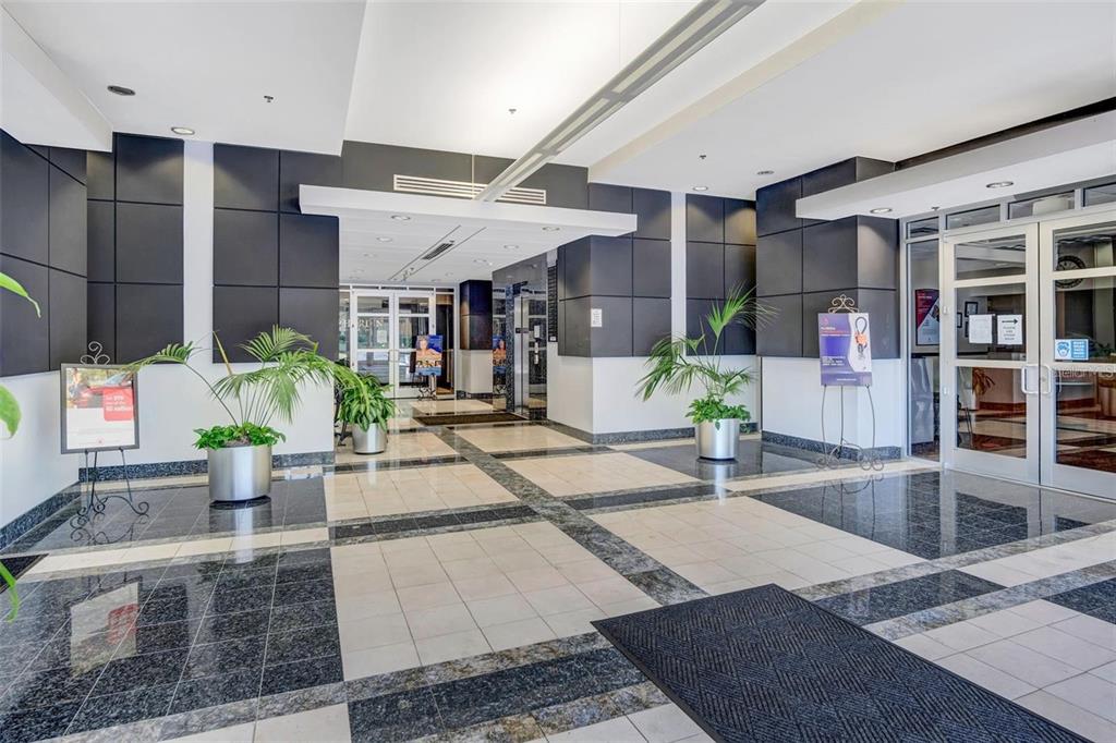 A modern building lobby features tiled floors, dark accent walls, and potted plants — 6200 METROWEST BOULEVARD UNIT 103B, ORLANDO, FL