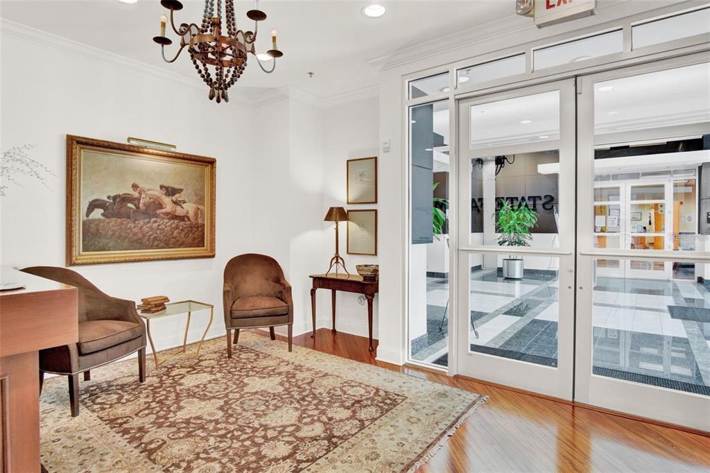 A lobby features two brown armchairs, a patterned rug, a chandelier, and glass entry doors — 6200 METROWEST BOULEVARD UNIT 103B, ORLANDO, FL