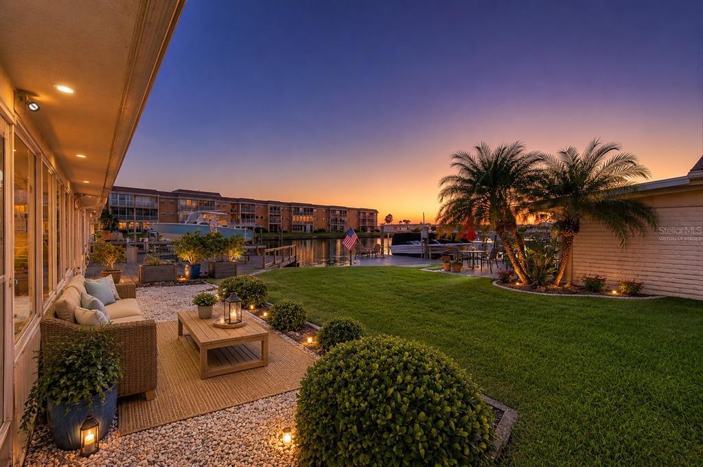 A view of a canal at sunset with wooden docks, boats, and a multi-story apartment building — 144 BOCA CIEGA POINT BOULEVARD N, ST PETERSBURG, FL
