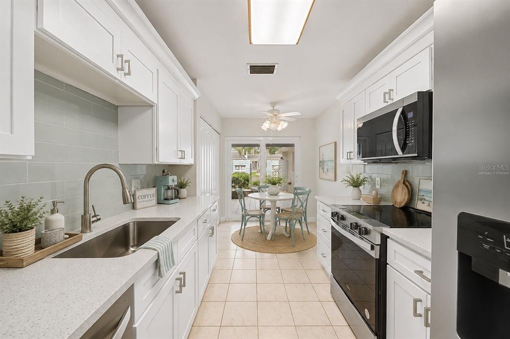A galley kitchen features white cabinets, quartz countertops, a gray subway tile backsplash, and stainless appliances — 144 BOCA CIEGA POINT BOULEVARD N, ST PETERSBURG, FL
