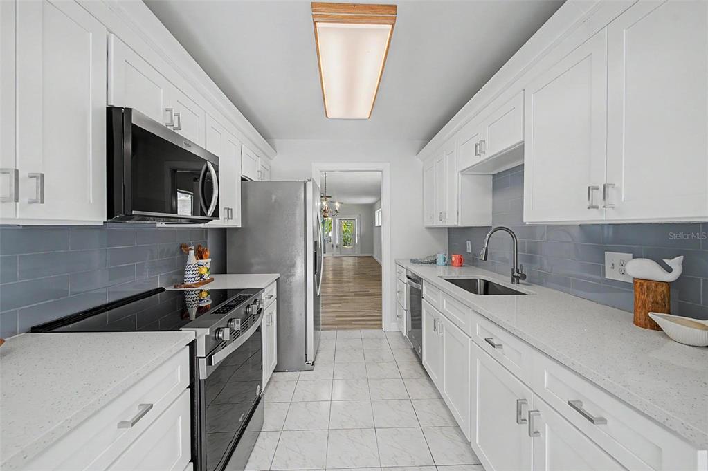 A kitchen with white cabinets, gray subway tile backsplash, quartz countertops, and a sliding glass door — 144 BOCA CIEGA POINT BOULEVARD N, ST PETERSBURG, FL