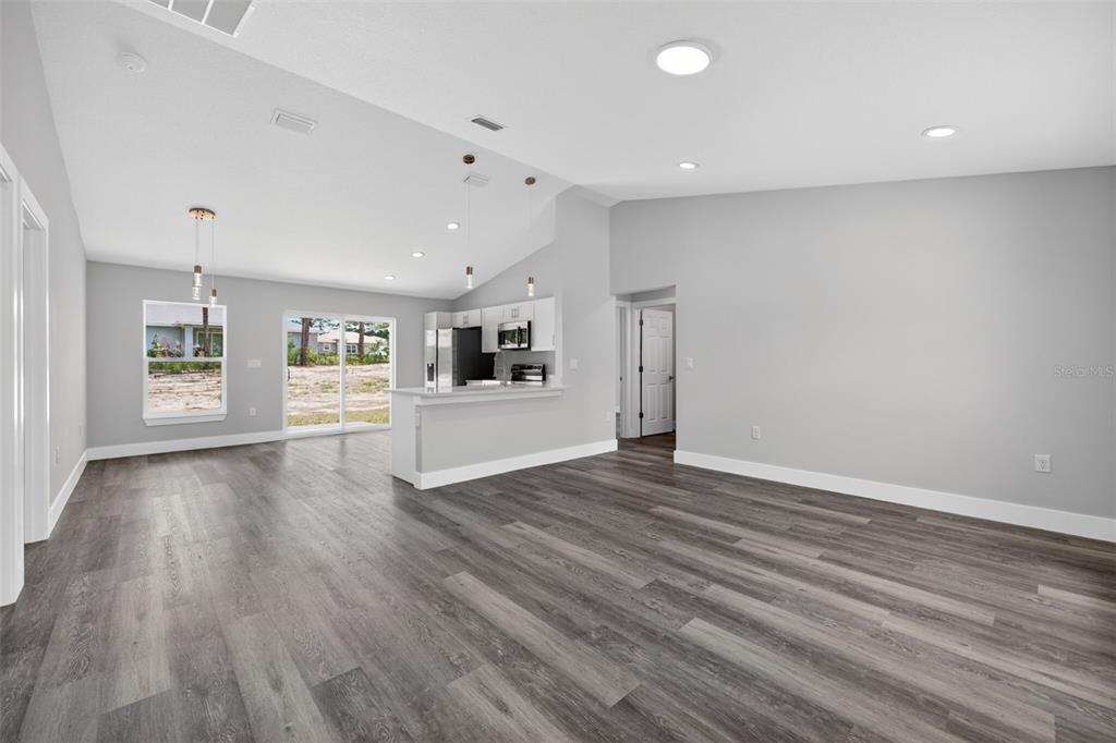 An open-concept living area features gray wood-look flooring, a kitchen island, and sliding glass doors — 13155 SW 70TH COURT, OCALA, FL