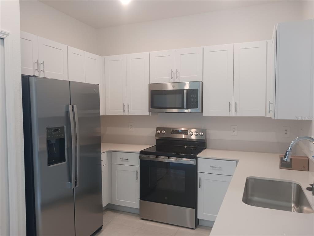 A kitchen features white cabinets, stainless steel appliances, and light-colored countertops — 8607 TROPICAL AIRE LANE, PARRISH, FL
