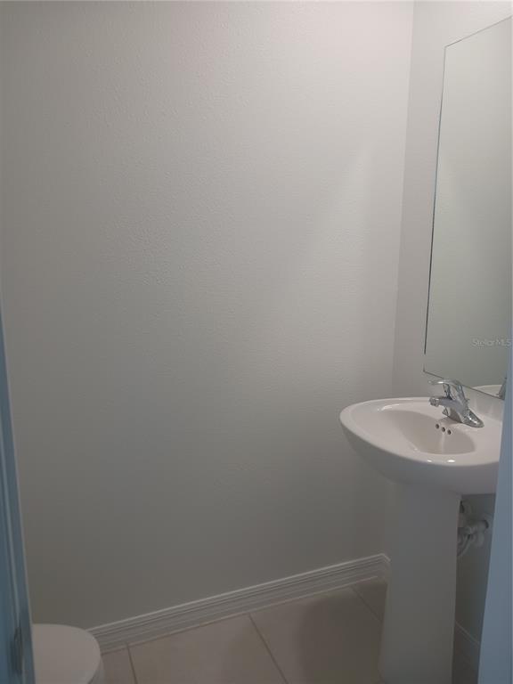 A small half bathroom features a white pedestal sink, a mirror, and light-colored tile flooring — 8607 TROPICAL AIRE LANE, PARRISH, FL