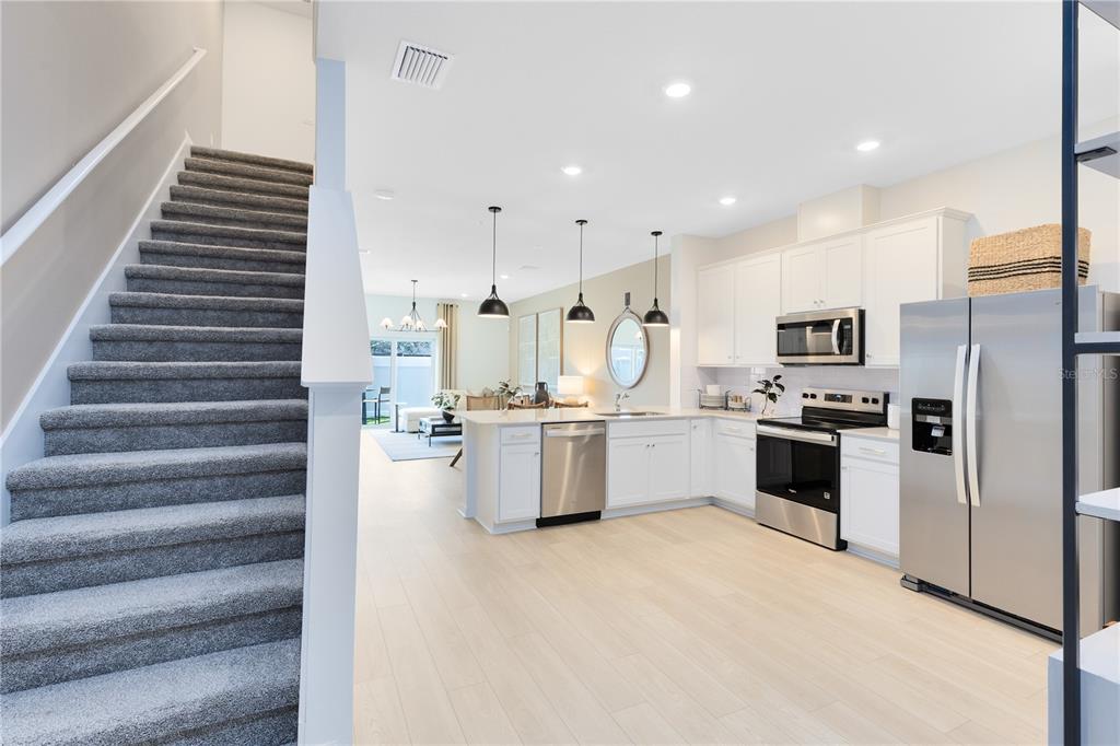 A carpeted staircase leads to an open-concept kitchen with white cabinets and stainless steel appliances — 4329 JETTY LANE NE, PALM BAY, FL