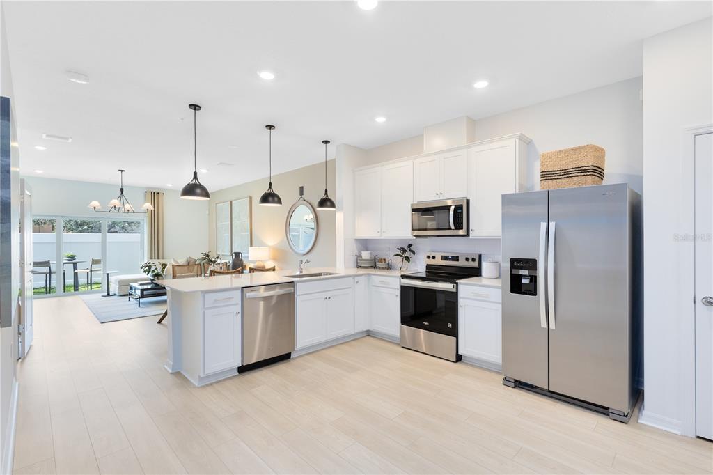 A modern kitchen with white cabinets, stainless steel appliances, and an island overlooks a living area — 4329 JETTY LANE NE, PALM BAY, FL