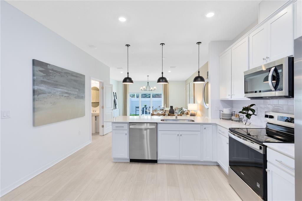 A modern kitchen features white cabinetry, stainless steel appliances, and a large island with pendant lighting — 4329 JETTY LANE NE, PALM BAY, FL