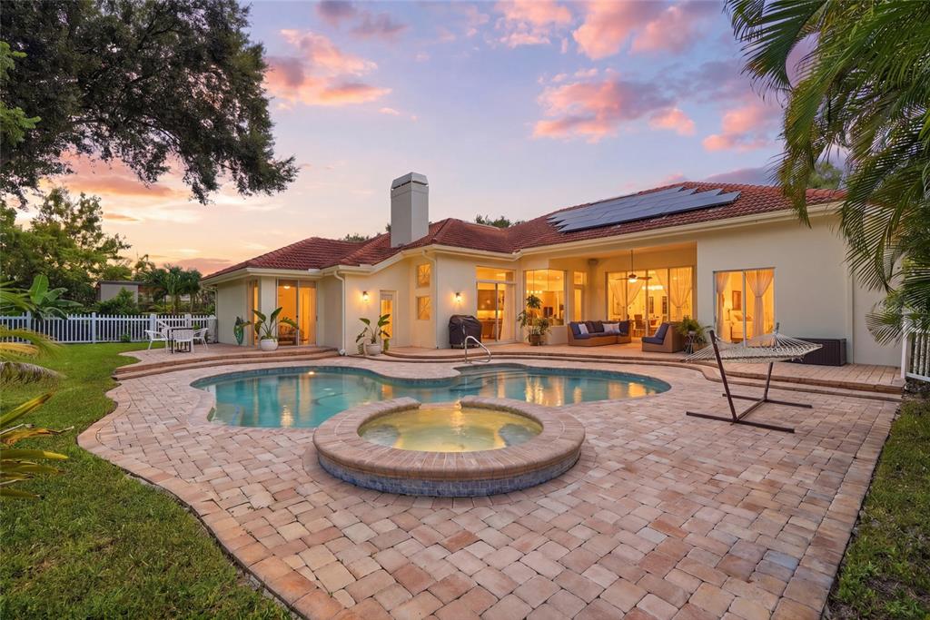 A backyard patio features a swimming pool, a raised hot tub, and a hammock at sunset — 3459 WOODRIDGE PARKWAY, PALM HARBOR, FL