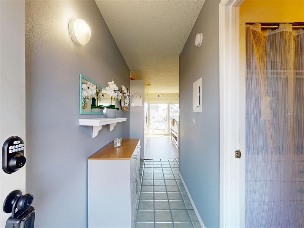 A hallway features a white console table, a wall-mounted shelf, and a mirror with a teal frame — 3700 S ATLANTIC AVENUE UNIT 103, NEW SMYRNA BEACH, FL