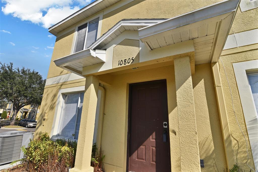 The exterior of a yellow stucco building features a covered entryway with a brown door — 10805 KEYS GATE DRIVE, RIVERVIEW, FL