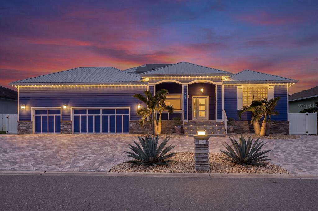 A blue house with a metal roof, stone accents, and a paved driveway at sunset — 704 EAGLE LANE, APOLLO BEACH, FL