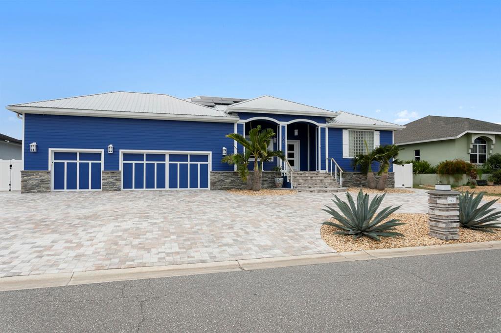 A blue house with a white metal roof and a paved driveway sits under a sky — 704 EAGLE LANE, APOLLO BEACH, FL