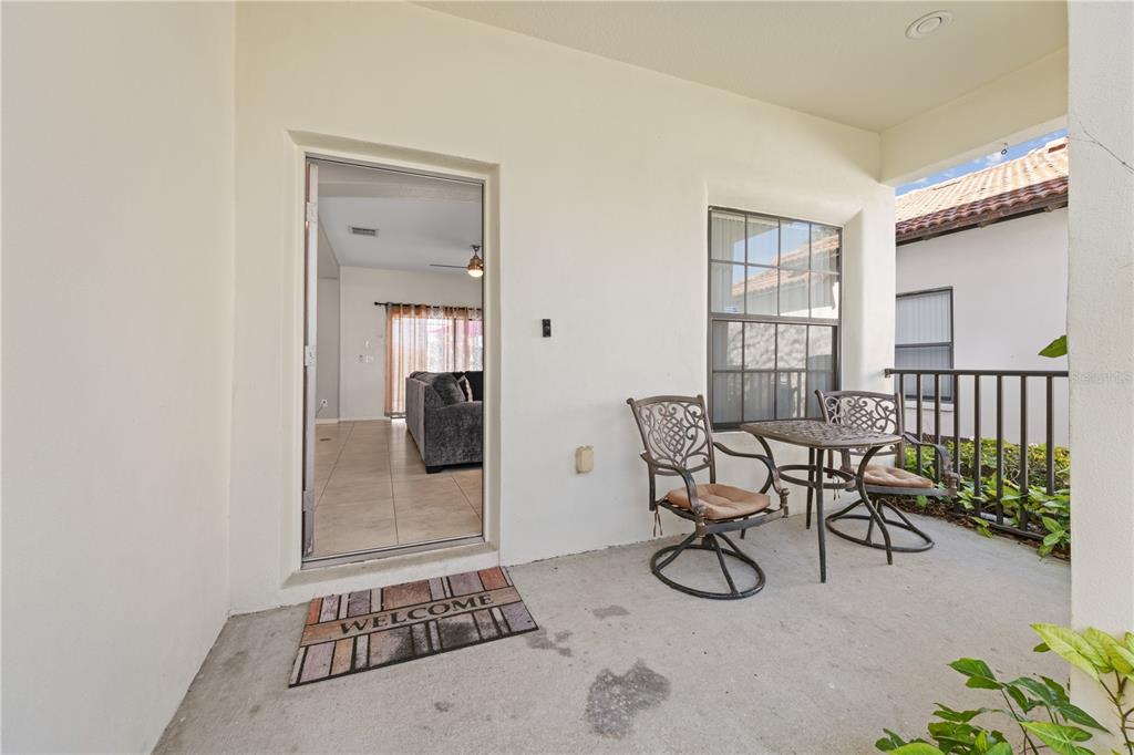 A covered patio features a concrete floor, a small metal bistro set, and a doorway — 114 SUMMER PLACE LOOP, CLERMONT, FL