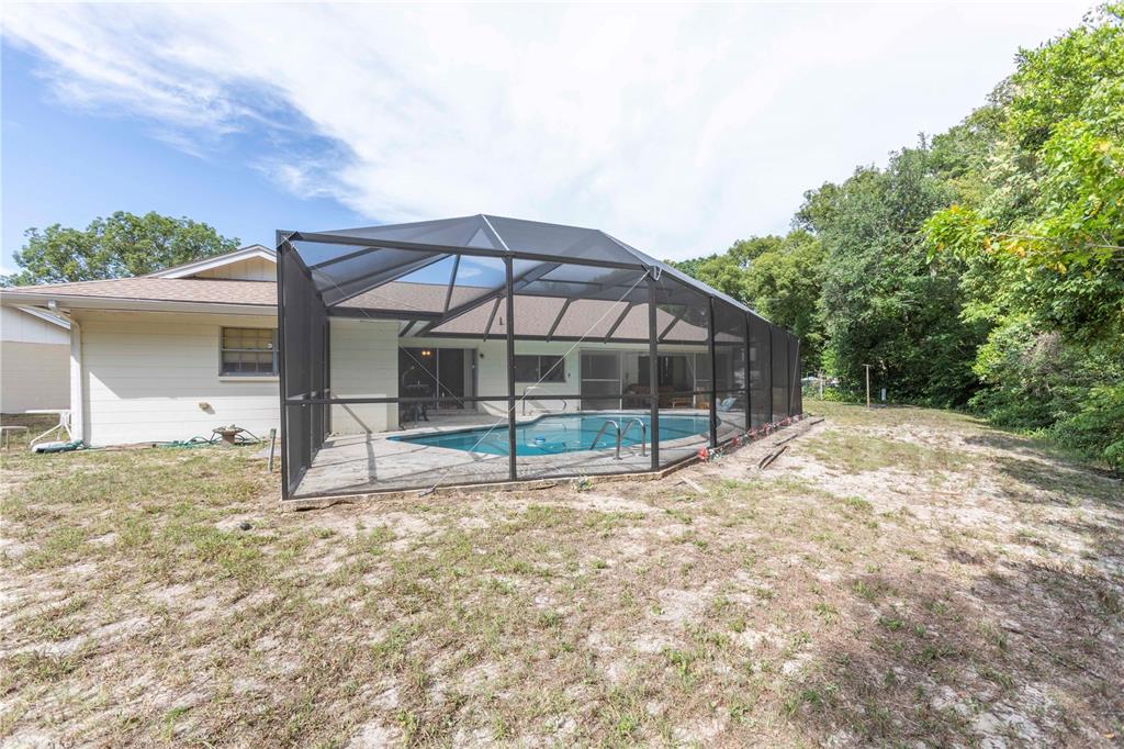 A backyard view of a house with a screened-in swimming pool and sandy lawn — 12101 LONGSTRAP LANE, HUDSON, FL