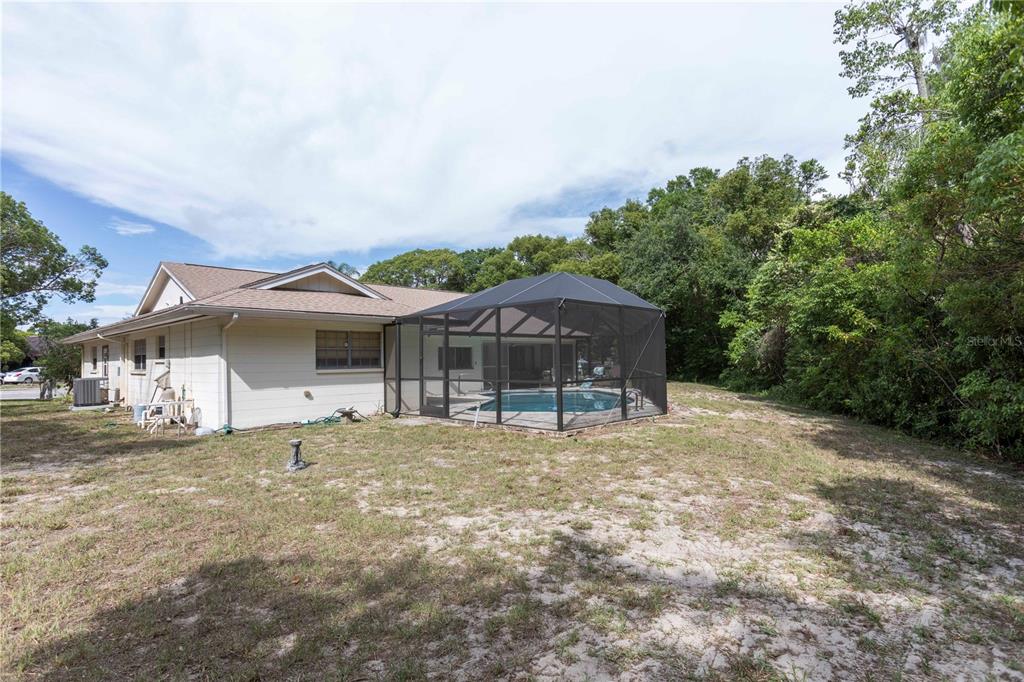 A house with a screened-in pool enclosure sits on a sandy lot near trees — 12101 LONGSTRAP LANE, HUDSON, FL