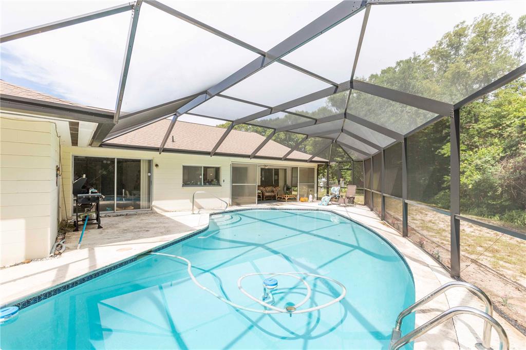 A swimming pool with a screen enclosure sits on a patio behind a house — 12101 LONGSTRAP LANE, HUDSON, FL