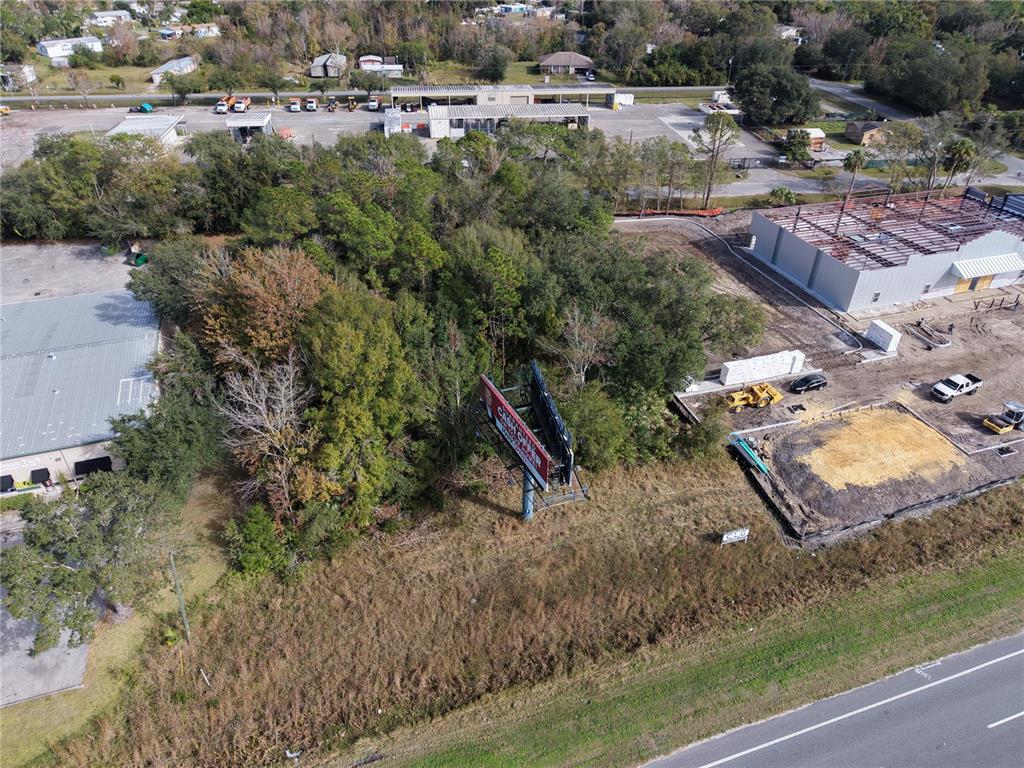 An aerial view shows a vacant, wooded lot with a billboard next to a construction site — E COLONIAL DR, ORLANDO, FL