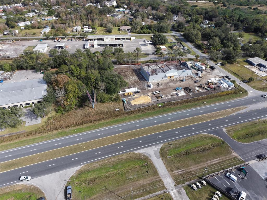 An aerial view shows a construction site with a steel-framed building next to a highway — E COLONIAL DR, ORLANDO, FL