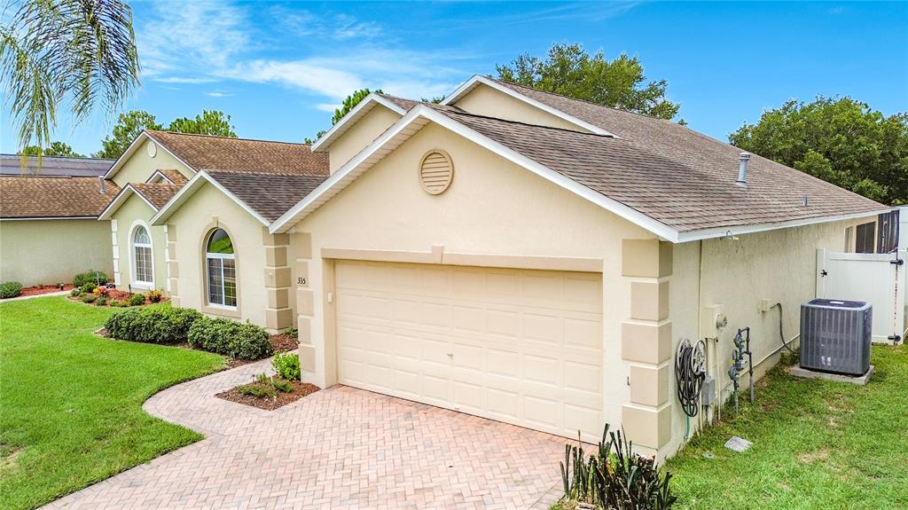 A beige single-story house with a two-car garage, brick paver driveway, and a shingled roof — 335 REGENCY STREET, DAVENPORT, FL