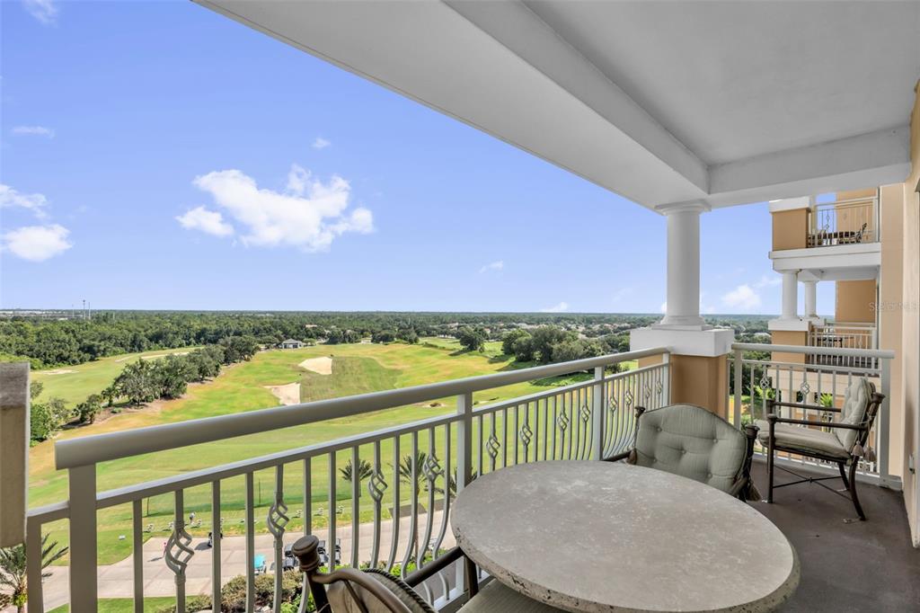 A balcony with a stone table and chairs overlooks a golf course under a blue sky — 7593 GATHERING DRIVE UNIT 707, REUNION, FL