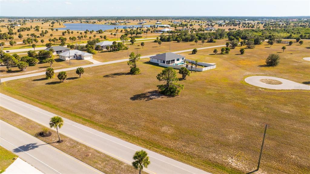 An aerial view shows a vacant grassy lot with scattered trees near a paved road — 99 HARNESS ROAD, PLACIDA, FL
