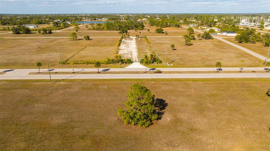 An aerial view shows a large, grassy vacant lot with a central tree and road — 99 HARNESS ROAD, PLACIDA, FL