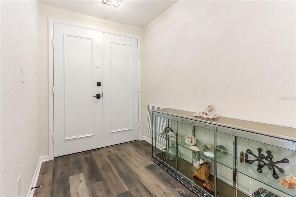 An entryway features white double doors, wood-look flooring, and a glass display console table — 4 BELLEVIEW BOULEVARD UNIT 205, BELLEAIR, FL