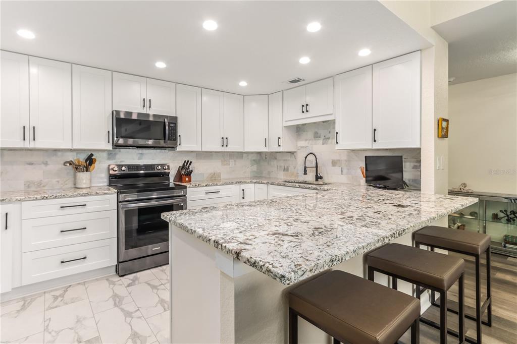 A white kitchen features granite countertops, stainless steel appliances, and a breakfast bar with stools — 4 BELLEVIEW BOULEVARD UNIT 205, BELLEAIR, FL