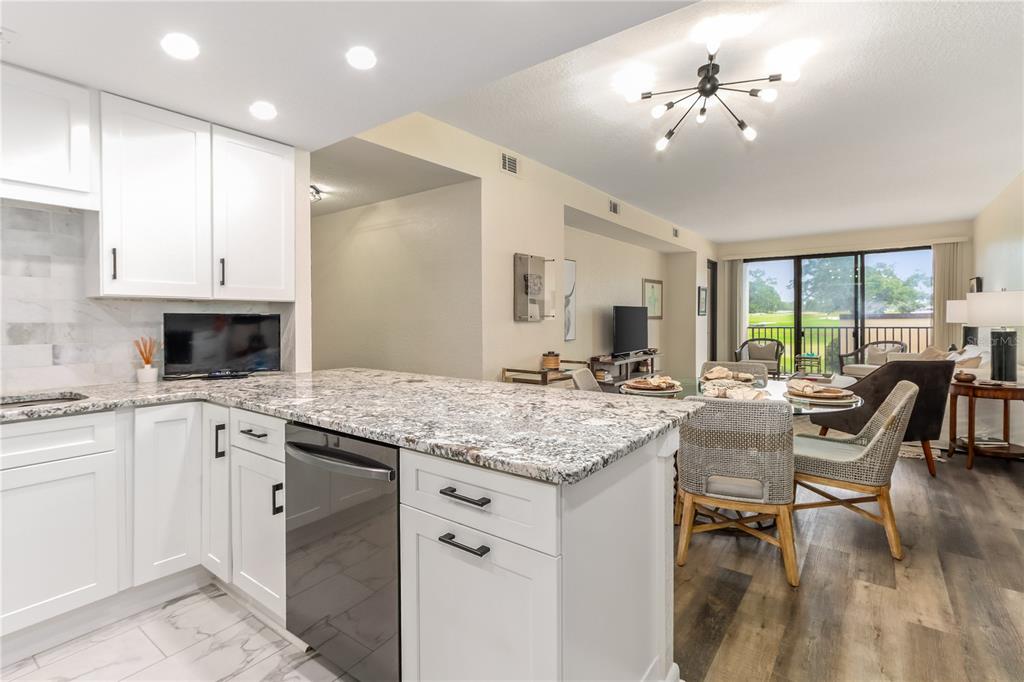 A kitchen with white cabinets and granite countertops overlooks a dining area and living room — 4 BELLEVIEW BOULEVARD UNIT 205, BELLEAIR, FL