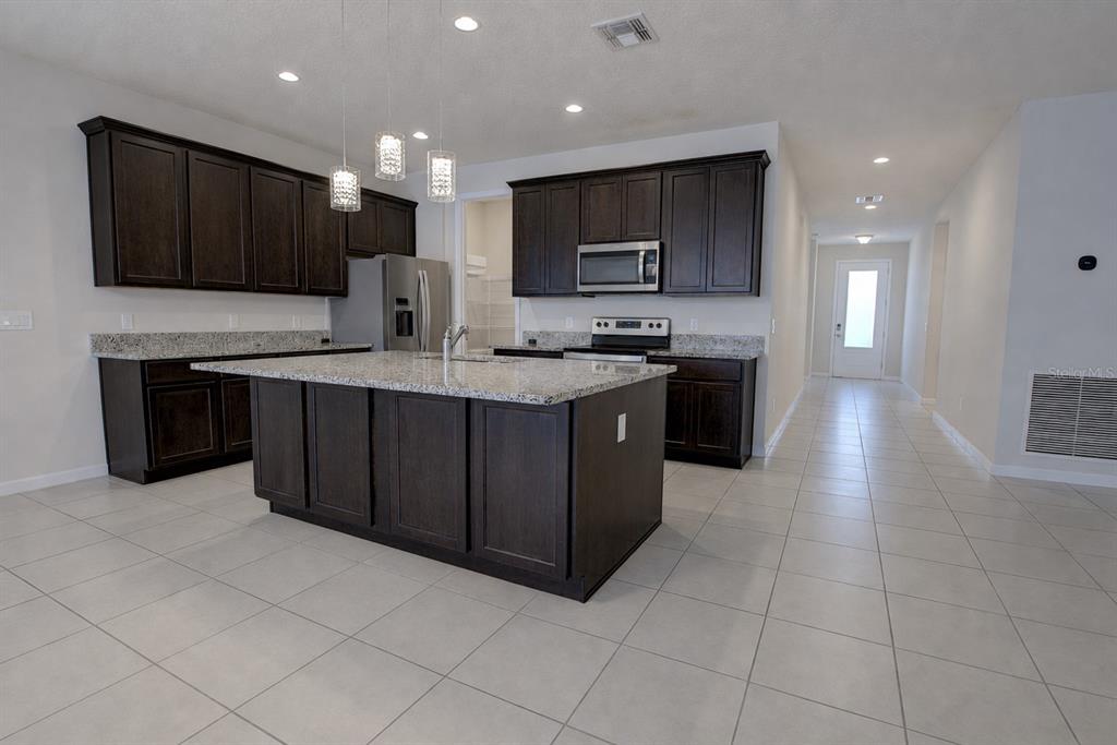 A kitchen features dark wood cabinets, granite countertops, a central island, and tile flooring — 3552 STONEBRIAR LANE, SANFORD, FL